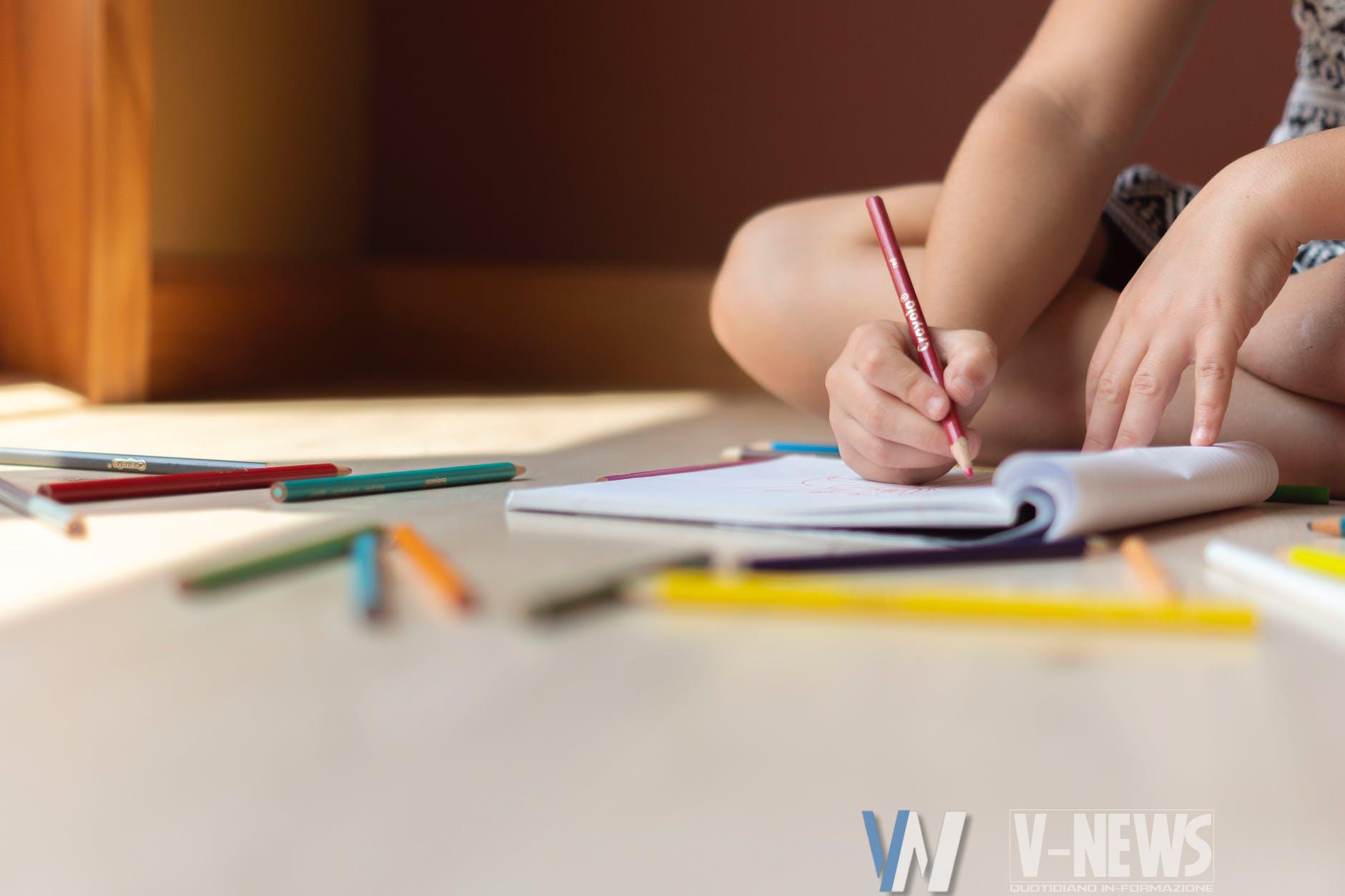 crop kid sitting on floor and writing in notebook